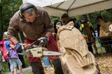 Linkziel: Link zum Beitrag mit dem Thema Spektakulärer Floßbau zum Waldfest am Stausee Hohenfelden; Bildinhalt: Ein Mann sägt bei einer öffentlichen Veranstaltung mit einer Kettensäge an einem Baum eine Eule heraus