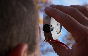 Ein Mann hält ein Messinstrument in der hand und schaut in Richtung Baumkrone