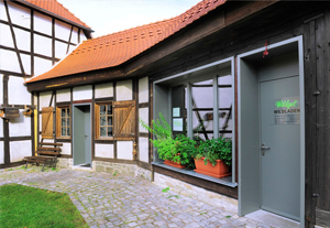 Blick auf einen kleinen mit Blumenkästen geschmückten Laden. Das Gebäude ist eingeschossig und im Fachwerkstil gebaut.