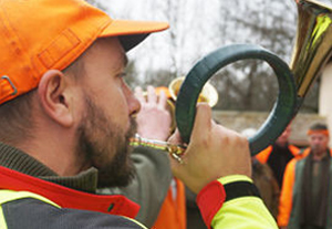 Junger Jäger mit orangefarbener Jagdkleidung bläst das Jagdhorn