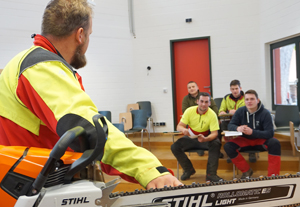 Kursleiter erklärt 4 Zuhörern die Funktionen einer Motorkettensäge
