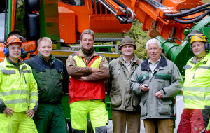 Gruppe freundlicher Menschen steht vor einem Forstfahrzeug zur Verkehrssicherung