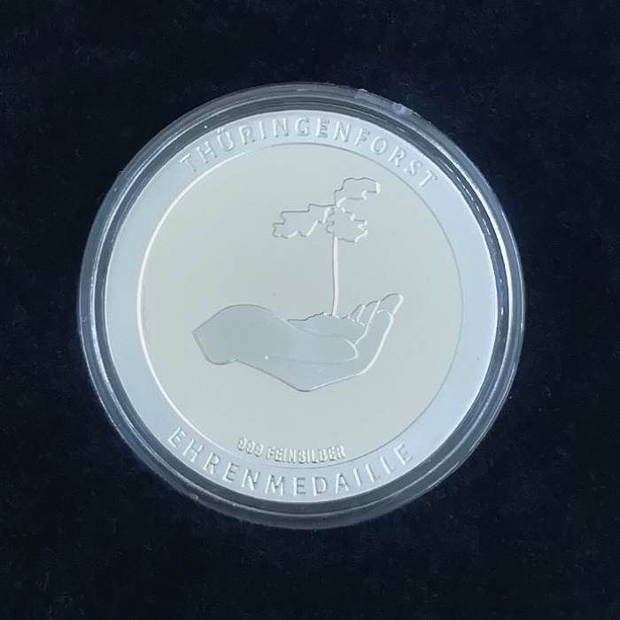 Rückansicht einer Silbermünze mit Prägung eine Hand mit einem Eichensetzling