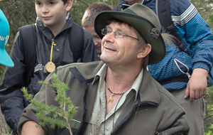 Ein Förster inmitten von Kindern einer Schulkasse. Der Förster erklärt der Klasse etwas an einem Nadelbaumzweig.