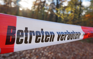 Absperrband mit der Aufschrift "Betreten verboten" zieht sich über einen Waldweg